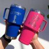 Dos manos sostienen vasos, uno azul y uno rosa, Termo personalizado clásico grande con agarradera 890ml 30oz con nombres y diseños decorativos para exteriores.