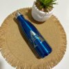 Termo personalizado botella 500ml 17oz azul y suculenta en maceta sobre mantelito redondo tejido con flecos, todo sobre una superficie blanca.