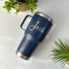 Un Termo personalizado clásico grande con agarradera 890ml 30oz, azul marino y con la etiqueta José, se encuentra sobre una mesa blanca rodeada de plantas verdes.
