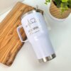 Termo personalizado clásico grande con agarradera 890ml 30oz, con grabado de enfermería, sobre tabla de madera junto a una maceta en una superficie blanca.