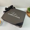 Caja personalizada con 2 diseños kraft mate, con texto "Feliz Cumpleaños" y listón negro, sobre superficie blanca junto a pequeñas plantas. Ideal para regalos especiales y celebraciones.