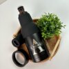 Un "Porta botellas y latas personalizado, con cuello y destapador" negro con la etiqueta El Morro se encuentra junto a una pequeña planta en maceta sobre una bandeja tejida.