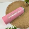 Termo personalizado delgado 590ml 20oz en rosa con “Nathalia” y un corazón en plateado, sobre un tapete tejido junto a plantas verdes—un lindo ejemplo de termos personalizados.