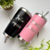 Dos vasos Termo personalizado clásico de 590 ml, uno negro y otro rosa con nombres grabados, se encuentran junto a una pequeña planta