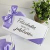 Caja personalizada con 2 diseños kraft mate, decorada con listón morado y la frase "Felicidades por tu jubilación" en la tapa, junto a una maceta.