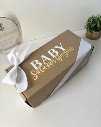 Caja personalizada con 2 diseños kraft mate, color marrón con lazo blanco y BABY Salazar Guyon en la tapa, se muestra junto a una pequeña planta en maceta.