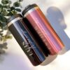 Dos vasos de viaje medianos personalizados de metal, cada uno con tapa, se encuentran en posición vertical. Uno de los vasos presenta un acabado oscuro con la palabra "LUIS" elegantemente escrita en blanco, mientras que el otro brilla en oro rosa y muestra la palabra "ESTHER" en una escritura a juego. Una ramita de eucalipto reposa junto a estos elegantes "Termo cilindro metalizado mediano personalizado 450ml 15oz" sobre un fondo claro.