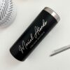 Un termo delgado personalizado negro de 590 ml y 20 oz muestra "Mariel Atando Cirujano Dentista" en una elegante letra cursiva blanca. Cerca de la superficie blanca, encontrará una pajita de metal y un objeto blanco texturizado.