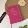 Libreta personalizada A5 lisa con elástico rosa, con "Profe: Tania" en español, acompañada de un bolígrafo y un artículo redondo de madera.
