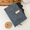 Dos elegantes Libretas personalizadas A5 con broche magnético metálico se asientan sobre un escritorio con una planta, una bandeja de madera y una caja redonda "Creatiboxs", cada una de ellas diseñada para guardar tus notas con seguridad y estilo.