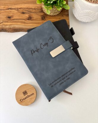 Dos elegantes Libretas personalizadas A5 con broche magnético metálico se asientan sobre un escritorio con una planta, una bandeja de madera y una caja redonda "Creatiboxs", cada una de ellas diseñada para guardar tus notas con seguridad y estilo.