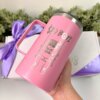 Una mano sostiene un Kit termo taza 710ml y caja chica personalizada de color rosa con la inscripción “$ADBOY” y una caricatura en un columpio; en el fondo, la caja de regalo personalizada está atada con una cinta violeta.