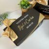 caja negra personalizada de regalo con moño dorado para peticion de padrinos de boda con texto en el exterior nuestra boda nombres y fecha