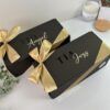 dos cajas color negro personalizadas con texto para padrinos y con moño color champaña