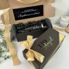 una caja color negro abierta y con mensaje en el interior para realizar peticion de padrinos y tiene como contenido un termo color negro personalizado con laser donde aparece el nombre del padrino y una caja color negro cerrada con moño y texto personalizado tio Angel