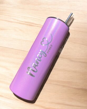 Un vaso de acero inoxidable adornado con purpurina violeta descansa sobre una superficie de madera. Muestra el nombre Nancy Pérez en texto metálico junto con un diseño de corazón y tiene una capacidad de 590 ml. Una pajita de metal se extiende desde la tapa, lo que le suma un toque distintivo a este Termo personalizado con purpurina de 590 ml y 20 oz.