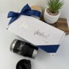 Kit termo portalatas 420ml y caja chica personalizada en color blanco, con texto ¡Feliz cumpleaños!, listón azul, vaso tipo tumbler, planta y tapa de madera sobre una mesa.