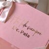 Una caja de regalo rosa con una cinta blanca que incluye un texto dorado que dice A tu lado siempre y Lic. Pala. El logotipo Creatiboxs está impreso en blanco en la esquina inferior de la caja.