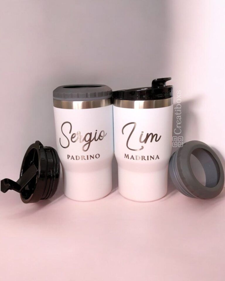 Se muestran dos tazas de viaje blancas con tapas negras. La taza de la izquierda dice Sergio en cursiva, Padrino debajo. La taza de la derecha dice Lim en cursiva, Madrina debajo. Dos tapas negras adicionales se colocan en la superficie junto a las tazas.