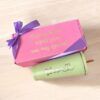 Una caja de regalo rosa con un lazo violeta se encuentra junto a un vaso verde. La caja tiene un texto en español que dice Después de este regalo serás aún más especial. El vaso muestra el nombre Blanca con un diseño de corazón.