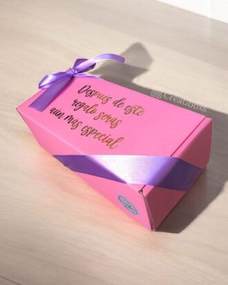 Sobre una superficie de madera clara se coloca una caja de regalo rosa con una cinta violeta. La caja tiene letras doradas que dicen: Después de este regalo serás aún más especial.