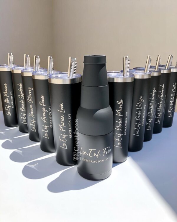 Una fila de termos de graduación personalizados (vasos negros y una botella con texto blanco personalizado) sobre una superficie blanca, ideales como obsequios de graduación considerados.