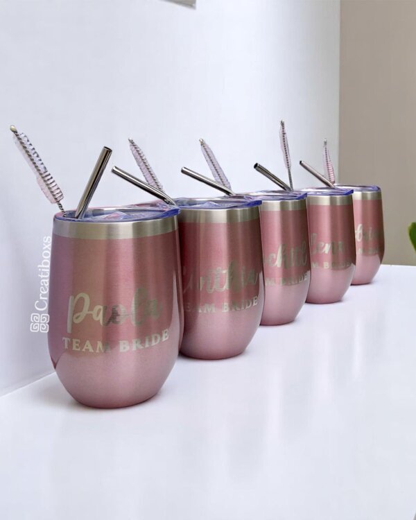 Cinco "Termos personalizados para boda" metálicos de color rosa con pajitas de metal, cada uno etiquetado como TEAM BRIDE, alineados sobre una superficie blanca, ideales para las celebraciones de tu boda.