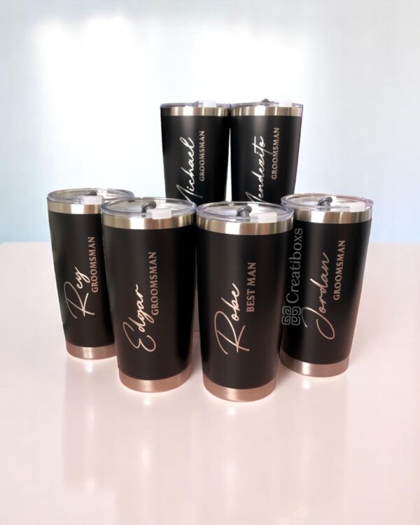 Siete termos negros personalizados para boda etiquetados como “Best Man” y “Groomsman” con nombres únicos, dispuestos sobre una superficie blanca: recuerdos de boda ideales para su día especial.