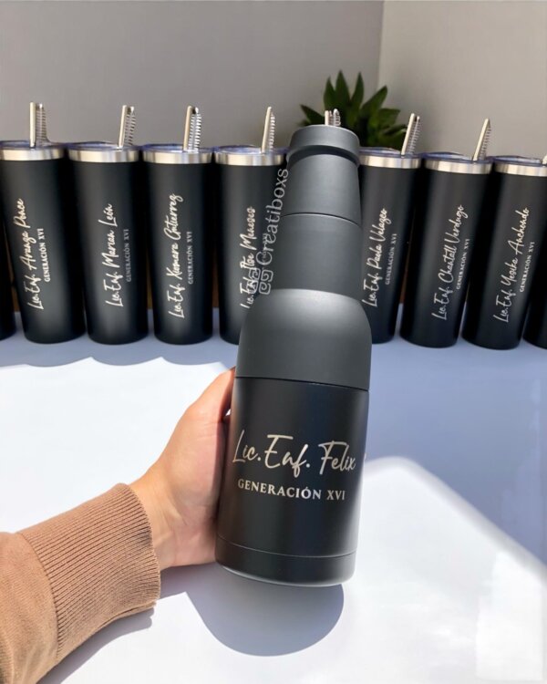 Una mano sostiene un termo de graduación personalizado en color negro; varios vasos a juego están alineados detrás, lo que los convierte en regalos de graduación ideales.