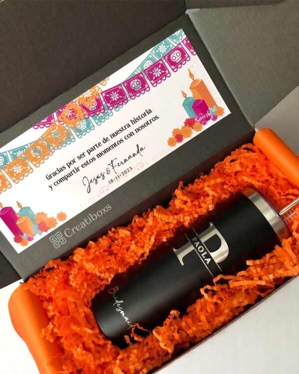 Termos personalizados para boda en una caja de regalo con papel naranja, una tarjeta festiva y papel picado colorido: detalles perfectos para cualquier celebración de boda.