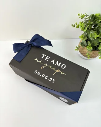 El Kit termo grande c/agarradera 890ml y caja chica personalizada viene en una caja de regalo negra con cinta azul marino, texto dorado y blanco y un fondo de planta en maceta, ideal para regalar o crear tu propio kit personalizado.