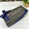 Una caja personalizada negra etiquetada con logo con un liston azul marino se encuentra sobre una superficie blanca cerca de plantas, ideal para regalar el Kit termo grande con agarradera 890ml y caja chica personalizada.