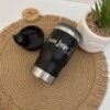 Termo personalizado portalatas 4 En 1 con destapador 420ml 14oz en negro con texto 'Anna Luiza', colocado al lado de una planta sobre una alfombra tejida.