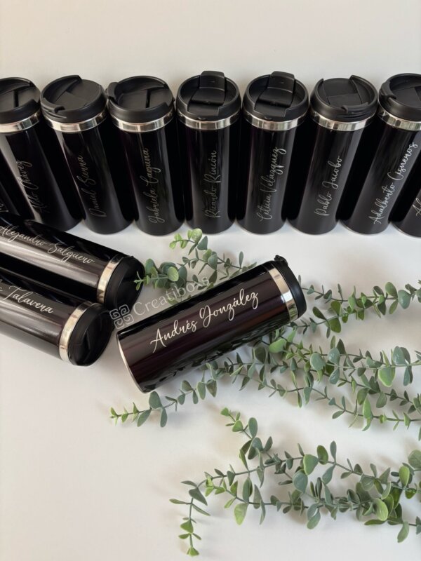 Nueve Termos personalizados para regalo de graduación en negro con nombres escritos, un vaso acostado, exhibido con vegetación, perfecto como regalo de graduación.