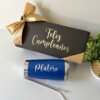 Pequeña caja de regalo personalizada con la etiqueta "Feliz Cumpleaños" y un lazo dorado, que incluye el vaso Platero Kit termo clásico de 590 ml y una pajita de metal, todo organizado en una elegante caja chica personalizada.