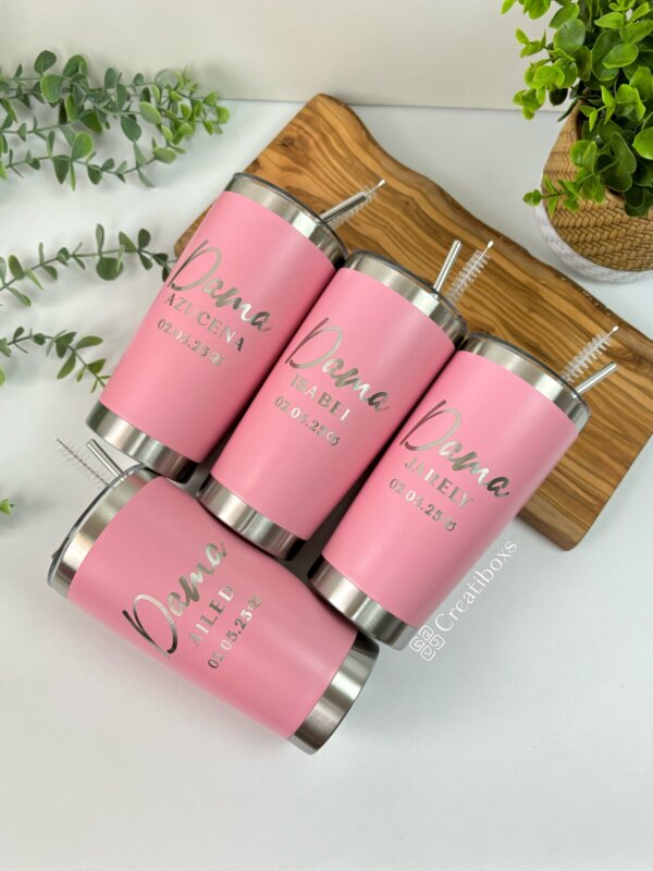 Cuatro termos personalizados para boda con rol de damas de honor o bridesmaids, en color rosa con pajitas plateadas se encuentran en una bandeja de madera, rodeados de exuberantes plantas verdes, lo que los convierte en recuerdos de boda perfectos para su día especial.