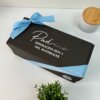 Caja de regalo negra con un lazo azul, etiquetada “Padrino Generación 2024-1 Ing. Materiales”, que presenta el Kit termo clásico grande 890ml y caja chica personalizada, exhibido sobre una mesa.