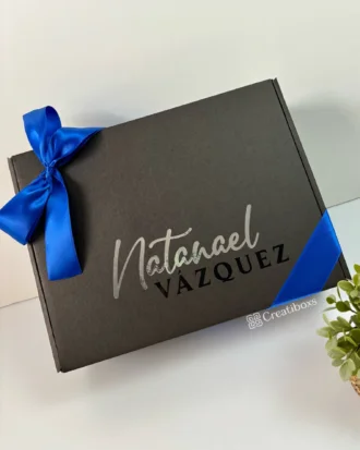 Set de regalo: Regalo personalizado para hombre con caja personalizada negra y lazo azul, etiqueta Natanael Vazquez, sobre fondo blanco. Incluye termo personalizado; perfecto para cualquier ocasión especial.