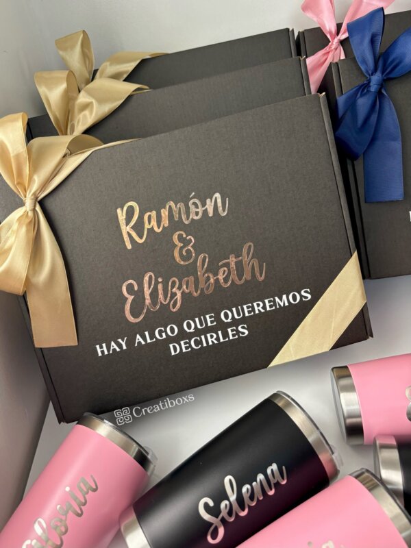 Caja de regalo para petición de padrinos en color negra con cinta dorada etiquetada como Ramón & Elizabeth y Termos personalizados para boda cerca, perfecta para que cualquier celebración de boda sea memorable.