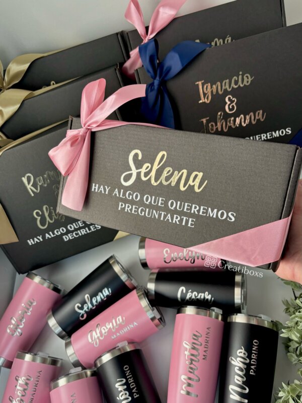Cajas de regalo para peticion de madrina y padrino con nombres en letras doradas, cintas rosas y doradas y termos personalizados para boda en negro y rosa: regalos personalizados perfectos para tu boda.