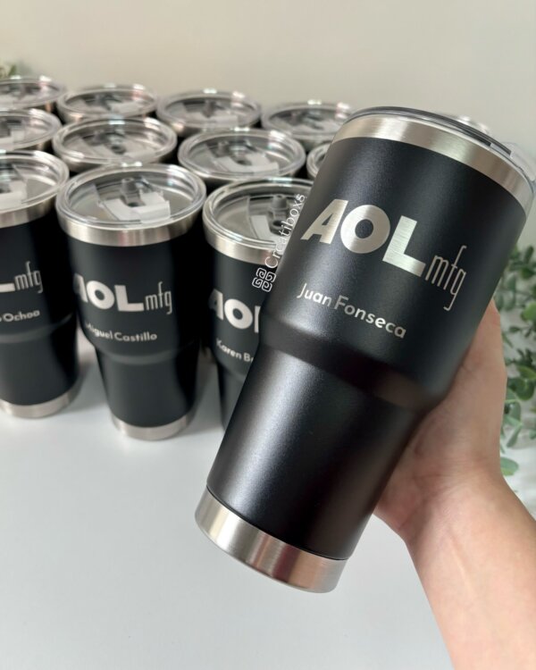 Mano sosteniendo un Termo personalizado para regalo corporativo con logo, con más termos personalizados con logotipos y nombres de la empresa en el fondo, ideal para regalos corporativos.