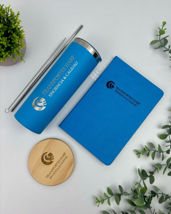 Termos personalizados para regalo corporativo con logo: incluye vaso azul, libreta azul, posavasos de madera y popote metálico sobre fondo blanco con plantas. Agrega tu logo y causa una impresión duradera.