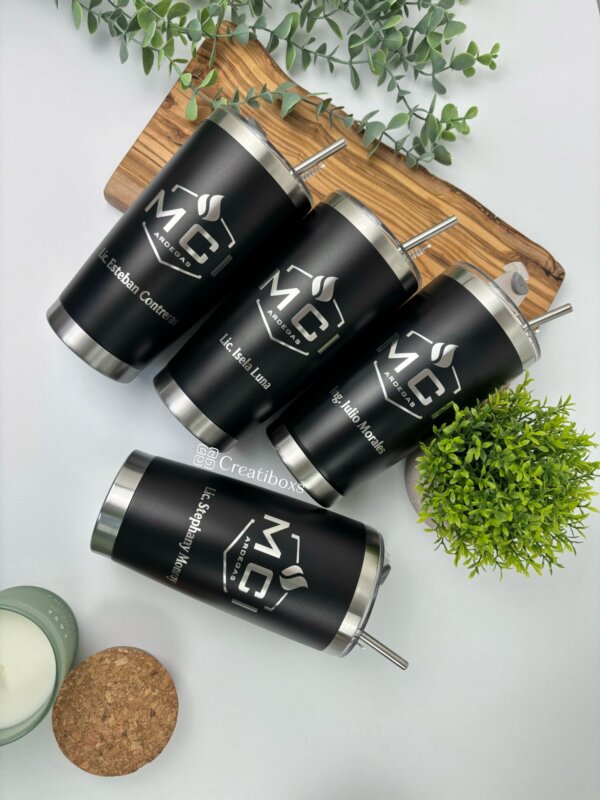 cuatro Termos personalizados para regalo corporativo con logo, en color negro con tapas y popotes plateados sobre una tabla de madera y plantas verdes, ideales como obsequio elegante para empresas.