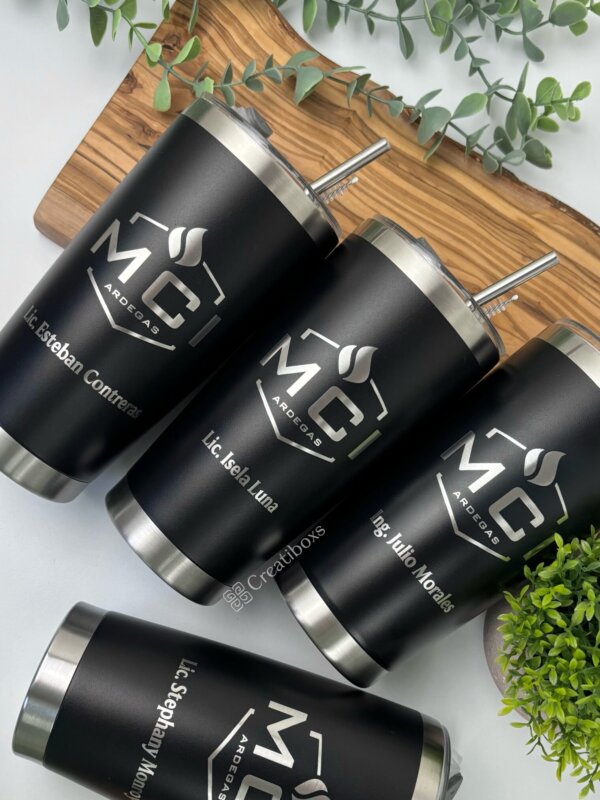 Cuatro termos personalizados para regalo corporativo con logo, de acero inoxidable negro y nombres grabados, rodeados de plantas verdes; el obsequio ideal para empresas.
