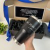 Una mano sostiene un termo clásico grande 890ml negro rotulado "LIC. JESUS" frente a una caja chica personalizada con mensaje en español y lazo azul, del kit termo clásico grande 890ml y caja chica personalizada.