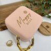 Joyero personalizado de cuero sintético mini en rosa con el nombre "Maggy Diaz" en letras doradas, junto a un anillo y una pulsera dorada sobre una superficie blanca.