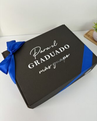 Caja personalizada con la frase "Para el graduado más guapo" en letra blanca y lazo azul, incluye un termo personalizado. Ideal como regalo de graduación.
