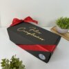 Caja de regalo negra con "Feliz Cumpleaños" en dorado, envuelta en cinta roja y rodeada de pequeñas plantas; incluye el Kit termo clásico 590ml y caja chica personalizada para un toque perfecto.