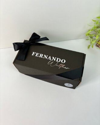 Un regalo personalizado para hombre con caja personalizada negra, lazo negro y nombre en la tapa, junto a una planta verde y un termo personalizado: el detalle ideal para cualquier ocasión.