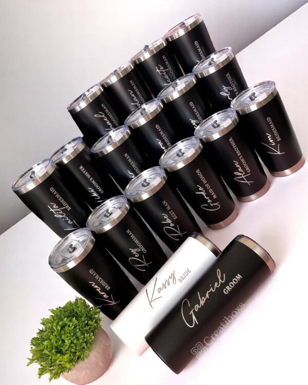 Termos personalizados para boda en blanco y negro dispuestos en una mesa junto a una pequeña planta verde—ideales como recuerdos únicos para tu celebración especial.